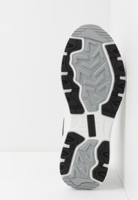 Suola di scarpa sportiva in bianco e nero con un motivo grigio testurizzato, caratterizzata da scanalature profonde per trazione e stabilità.