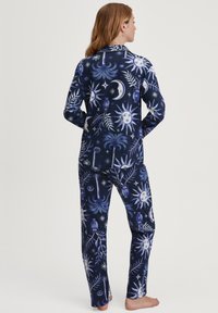 Marineblauw pyjama-set met hemelse patronen van zonnen en manen in blauw en wit. Gemaakt van zachte stof, inclusief langmouwtop en broeken.