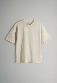 Kremowa koszulka z krótkim rękawem, okrągłym dekoltem, wykonana z miękkiej bawełny, charakteryzująca się luźnym krojem i minimalistycznym designem.