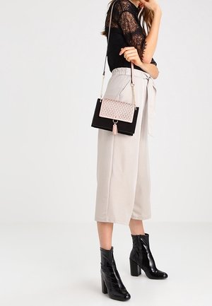 Czarna i różowa torebka na łańcuszku, wykonana z materiału przypominającego zamsz, o prostokątnym kształcie, z fakturowanym wzorem na przedniej części oraz ozdobą z frędzli.