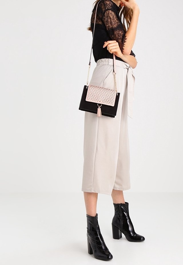 Svart och rosa handväska med kedjerem, mockaliknande material, rektangulär form, texturerat mönster på framsidan och tofsdetalj.