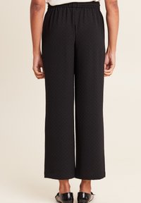Pantaloni neri a gamba larga con un motivo testurizzato, con vita elastica e una vestibilità ampia, progettati per comfort e facilità di movimento.