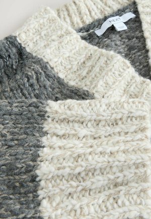 Krém és szürke színű, vastag, texturált fonalból készült, bulky kötött pulóver, amelynek a nyakában a következő felirat található: "NEXT".