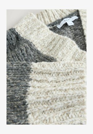 Chunky pletena pulover v kremni in sivi barvi z debelo, teksturirano prejo in etiketo z napisom "NEXT" znotraj ovratnika.
