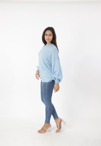 Suéter extragrande azul claro con tejido texturizado, costuras de hombro caídas; combinado con jeans ajustados azules y sandalias de tacón transparente.