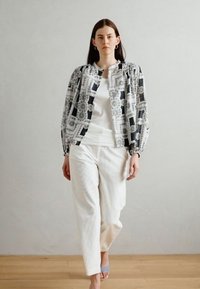 Giacca leggera a fantasia con maniche a sbuffo in nero, bianco e grigio, abbinata a una maglietta bianca semplice e pantaloni cremosi e testurizzati.