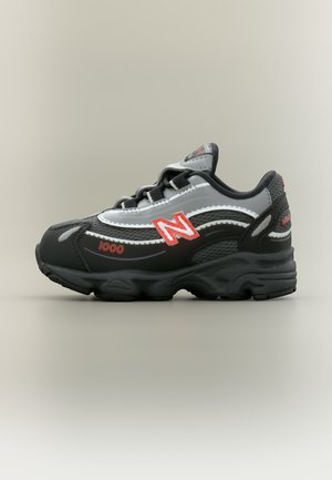 Sort og grå New Balance 1000 sneaker med rødt logo og tyk sål, vist fra siden på en ensartet lys baggrund.