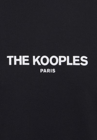 Svart stoff med hvit brodert tekst som leser "THE KOOPLES PARIS." Enkel, moderne design med en jevn tekstur.