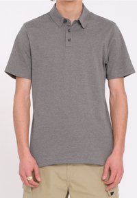 Polo gris à manches courtes avec un col, patte de boutonnage à trois boutons et un logo discret. Le tissu semble lisse avec une texture légère.