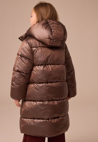 Manteau matelassé marron avec une capuche, présentant un design matelassé et une texture brillante. Il a des manches larges et est long jusqu'aux genoux.
