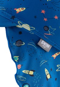 Blue swimwear fabric featuring a space theme with rockets, planets, and stars in assorted colors. Includes a "SWIM" tag. Soft texture.
