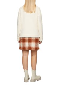 Crème sweatshirt, geruite rok in roest en beige, knie lengte, gestructureerde stof. Beige enkellaarsjes met dikke zolen en trekflappen.