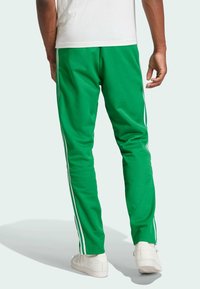 Pantalones deportivos verdes de tela suave con rayas laterales blancas. Diseño ajustado con cintura y puños elásticos, combinados con zapatillas blancas.