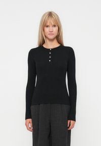 Bluză neagră cu mânecă lungă, cu design cu striații, decolteu rotund și cinci butoane decorative la închidere. Asortată cu pantaloni largi și închiși la culoare.