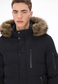 Sort pufferjakke med en hætte foret med pels, udstyret med lynlåslommer, trykknapper og en tekstureret finish.
