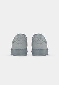 Sivi Nike Air Force 1 tenisice s glatkom teksturom, zaobljenim petom i uzdignutim logotipom na stražnjem dijelu. Gumeni potplat.