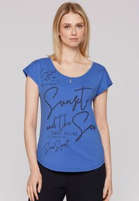 Blauwe T-shirt met korte mouwen en een ronde halslijn, met zwarte bedrukte tekst en een klein sleutelgatdetail aan de voorkant.