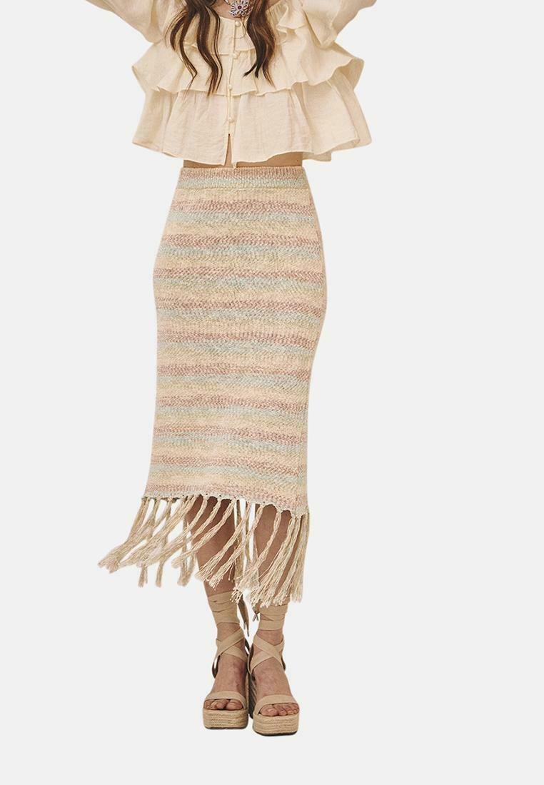 Falda de punto con rayas en tonos pastel, dobladillo con flecos y una silueta ajustada. Combinada con una blusa con volantes y sandalias de plataforma.