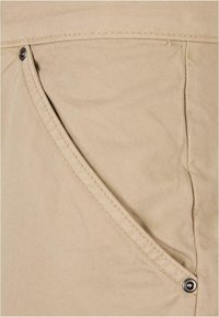Beige tkanina zblízka s zaoblenou kapsou a stříbrným patentním uzávěrem a jemnými texturovými liniemi.