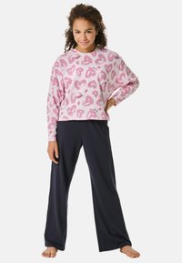 Roze langekleur shirt met hartpatronen, gecombineerd met zwarte wijde broek. Beide zijn gemaakt van zachte, comfortabele stof die geschikt is voor ontspannen.