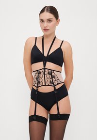 Črni komplet spodnjega perila, ki vključuje bralette, hlačke z visokim pasom in prosojen korzet z cvetličnim vezenjem ter nastavljivimi naramnicami.