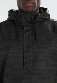 Anorak nero con cappuccio, dotato di un motivo camouflage testurizzato, con tasca a marsupio e cordini regolabili sul cappuccio.