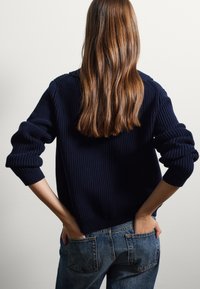 Marineblauer Rippstrickpullover mit überschnittenen Schultern, langen Ärmeln und umgeschlagenem Saum, kombiniert mit hochgeschnittenen blauen Jeans.