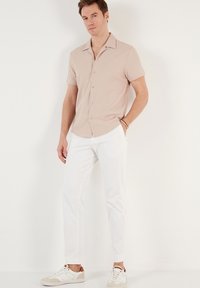 Camisa de manga corta de color beige con cuello acanalado, cierre de botones en el frente, combinada con pantalones blancos ajustados y zapatillas de color crema.