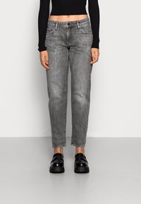 Šedé džíny ve střihu rovného střihu, s předními kapsami a zapínáním na knoflík. Nošeny s černými botami na platformě a krátkým topem s dlouhým rukávem.