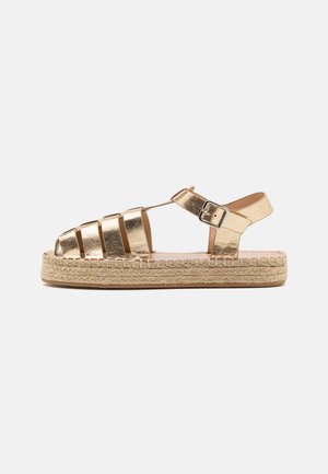 Guld metallisk strappy espadrille sandal med en flettet jute-sål og justerbar ankelspænde. Åben tå-design. Glat tekstur.