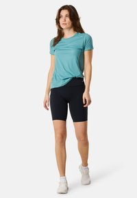 T-shirt azzurro chiaro traspirante abbinato a pantaloni bike neri a vita alta. Il modello indossa scarpe da ginnastica bianche con un leggero branding.