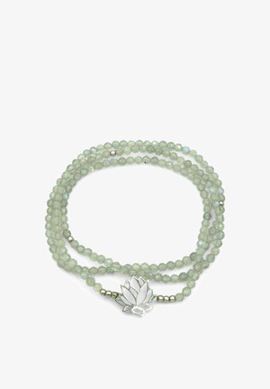 Collana di perle sfaccettate color verde chiaro con ciondolo a forma di fiore di loto in argento su uno sfondo bianco, disposta in un cerchio sciolto.