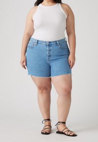 Shorts en denim bleu avec ourlet effiloché, design taille haute. Associés à un débardeur côtelé blanc et des sandales noires à brides.