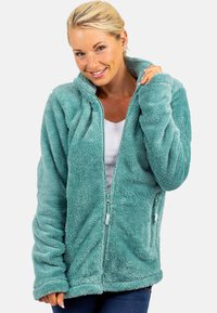 Giacca in pile felpato blu petrolio con zip frontale, colletto alto e tasche laterali. Tessuto morbido con una vestibilità rilassata e maniche lunghe.