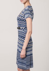 Niebieska i biała sukienka w wzory z zygzakowym wzorem, krótkimi rękawami i marszczoną talią z czarnym paskiem jako akcentem.