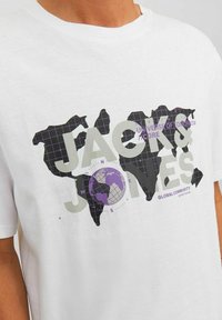 Camiseta blanca de algodón con un diseño gráfico de un mapa del mundo en negro con acentos morados y el texto "JACK & JONES" y "COMUNIDAD GLOBAL."