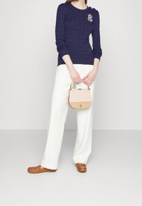 Marinblå kabelstickad tröja, vita vida byxor och en liten tvåfärgad handväska med guldfärgade detaljer. Tröjan har en logotyp och knappdetaljer.