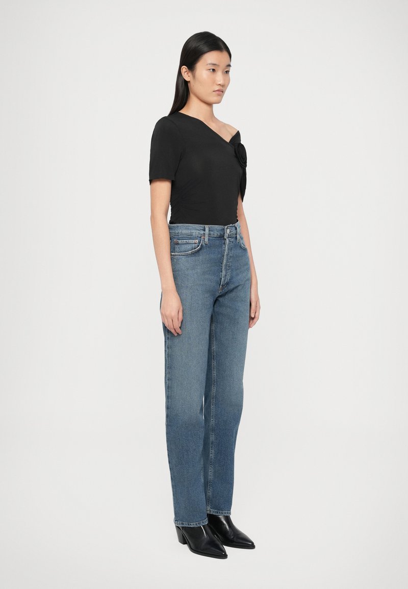Zwart aangesloten topje met een off-shoulder ontwerp en een bloemaccent, gecombineerd met lichtblauwe rechte jeans en zwarte enkellaarsjes met hak.