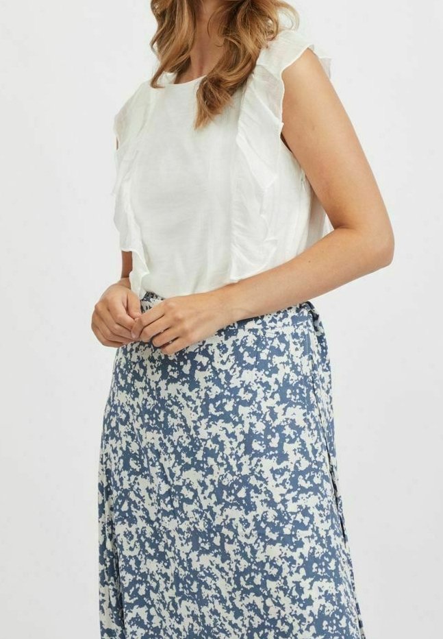 Bílý top s volánovými rukávy, kombinovaný s modrou sukní s květinovým vzorem. Sukně má světlé a tmavé modré akcenty na světlém pozadí.