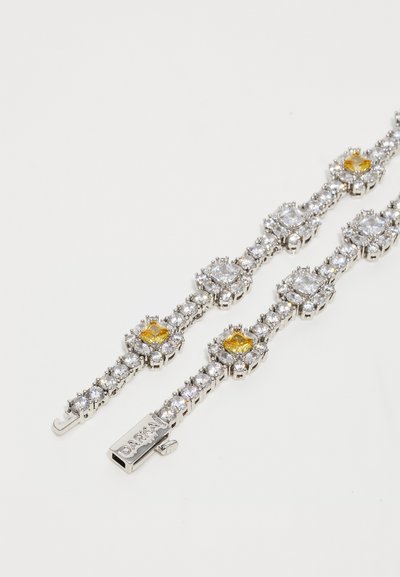 Silver-tone tennis bracelet with clear and yellow square-cut gemstones and a clasp engraved with "DANNIJO" on a white background.