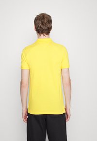 Polo shirt jaune à manches courtes et col, avec un ourlet droit et des fentes sur les côtés, fabriqué dans un tissu doux et léger.