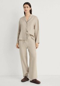 Beige linen pajama set featuring a button-up shirt with a notched collar and matching wide-leg pants. Soft texture, relaxed fit, minimal design.
