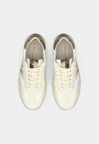 Ein Paar weiße und beige Damensneaker mit goldenen Akzenten, Schnürsenkeln und Markenlogo, von oben auf einem weißen Hintergrund betrachtet.