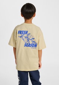 Beżowy bawełniany t-shirt z krótkimi rękawami, z niebieskim napisem graficznym "FRESH SEASON" i wzorem piłek nożnych oraz liści na plecach.