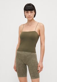 Top in verde oliva con spalline sottili, design aderente, texture liscia. Abbinato a pantaloni corti a coste in verde oliva, con lunghezza fino al ginocchio.