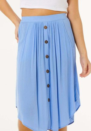 Højtaljet lyseblå midi-nederdel med træknapper foran, sidelommer, plisseringer og en let asymmetrisk kant, båret med en hvid cropped top.