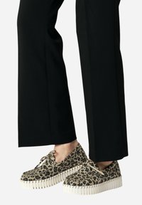 Zapatos de estampado de leopardo con una suela de goma blanca gruesa. Diseño de cordones, con un tejido texturizado y punta redonda. Combinados con pantalones negros.