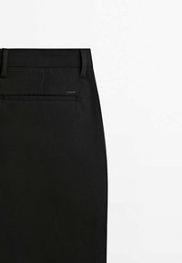 Musta hame, jossa on sileä pinta, takatasku ja vyölenkit. Yksinkertainen muotoilu ja siisti siluetti.