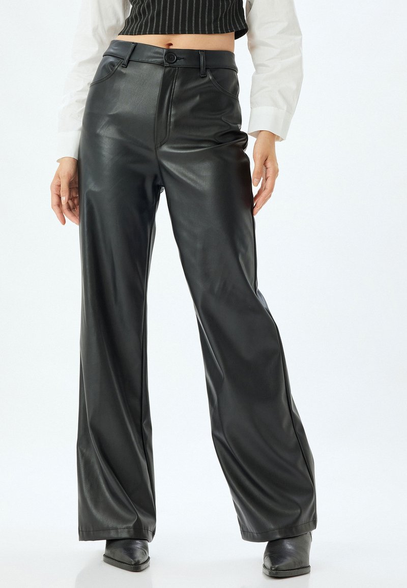 Zwarte faux leren wijde broek met een hoge taille, voorzakken en een gladde textuur. Voorzien van een enkele knopen sluiting en riemlussen.