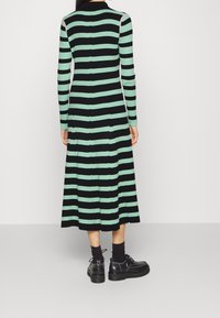 Abito in maglia con righe verticali nere e verde menta, maniche lunghe, colletto e orlo svasato. Abbinato a scarpe nere chunky e calze.